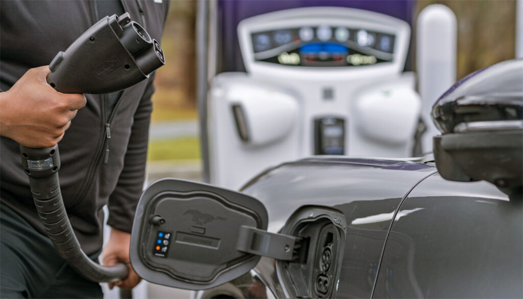 Closeup of an electric charging port on a car, and a person holding a charging device.