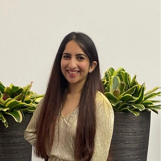 Person smiling with long hair wearing light color shirt in front of potted plants.