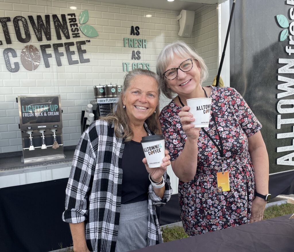 Two smiling women each holding an Alltown Fresh coffee